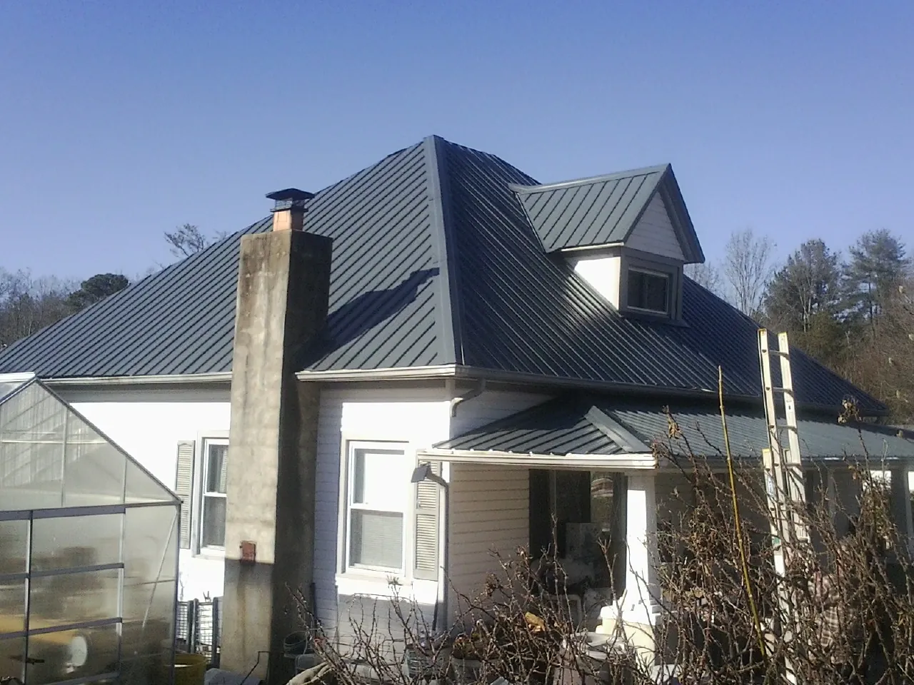 Dark blue standing seam metal roof on a white farmhouse with dormer — Slate & Tile Roof Repair by Roofing Brothers in Lakemore