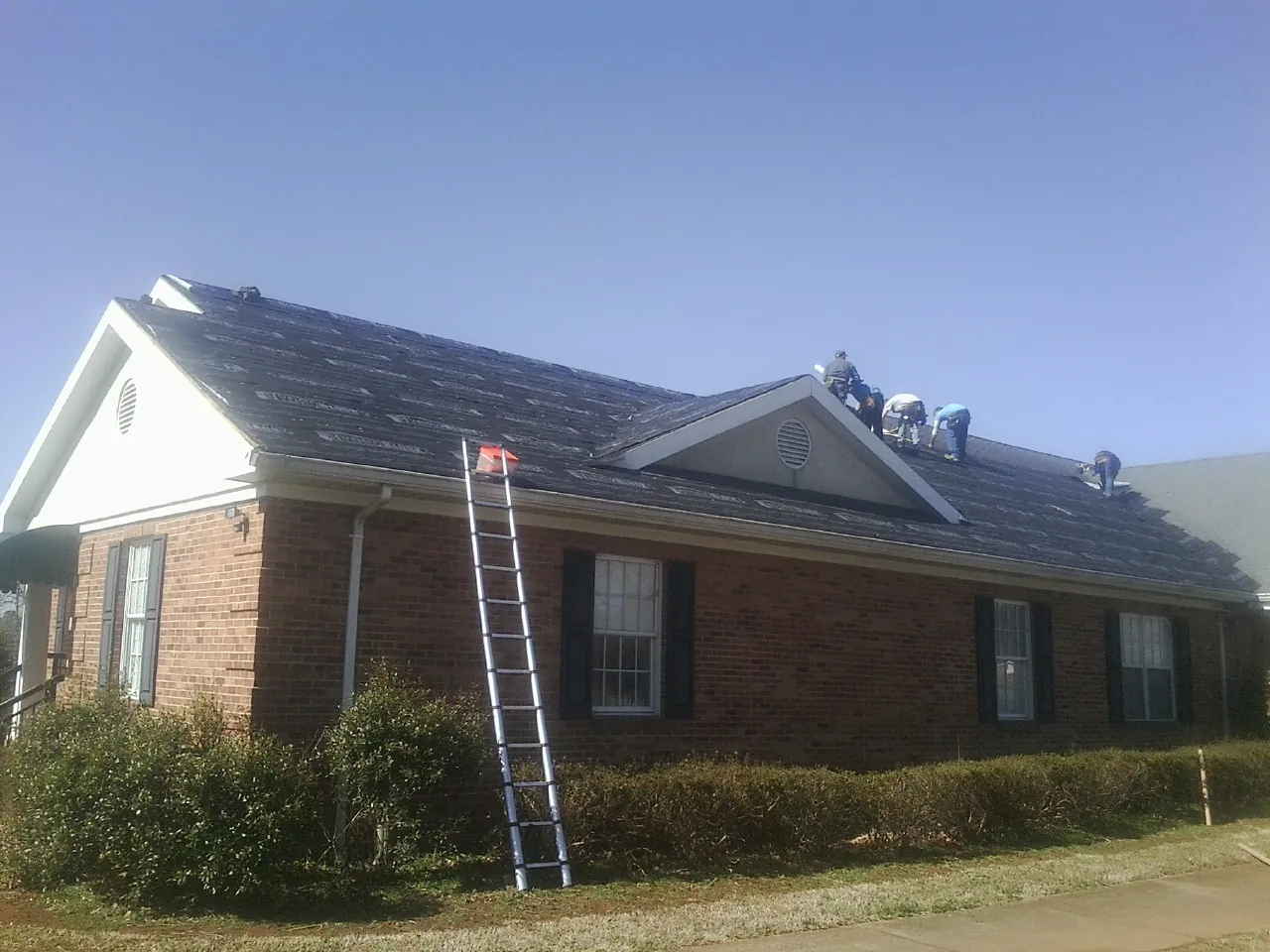 Crew tearing shingles off a brick ranch roof with a ladder set — Emergency Roof Repair work by our crew in Lakemore