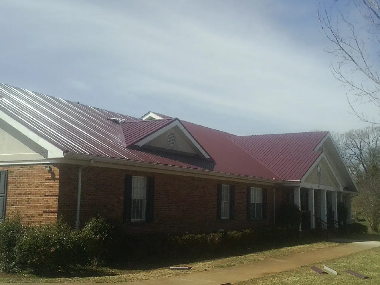 Red metal roof with gabled entries on a long brick building, from a Hail Damage Roof Repair job in Lakemore