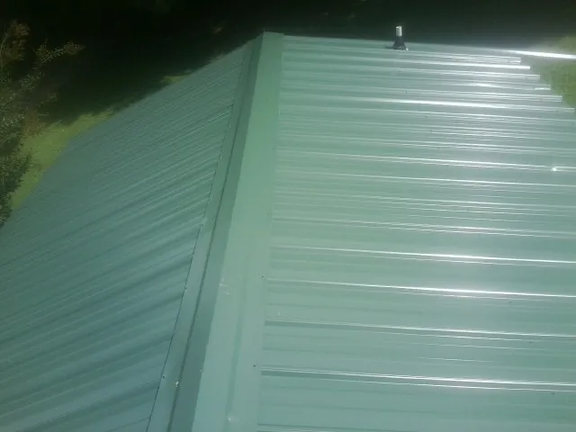 New green metal panels meeting at the ridge of a roof — Flat Roof Repair work by our crew in Lakemore