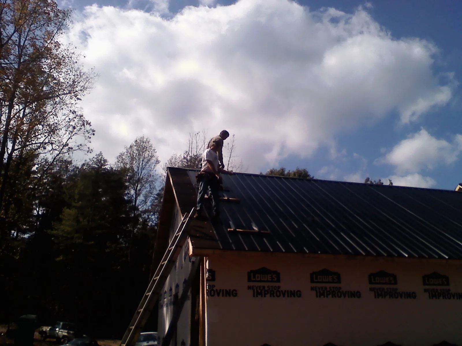 Roofer fastening dark metal panels high against a cloudy sky, from a Roof Inspection job in Lakemore