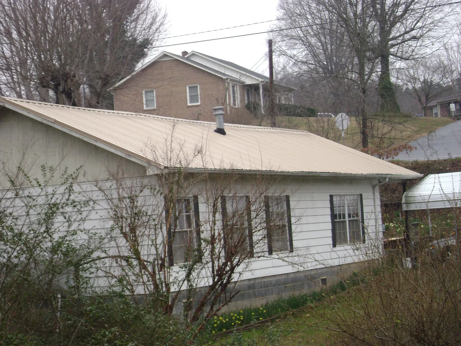 Tan metal roof on a white sided house set into a hillside — Commercial Roofing by Roofing Brothers in Lakemore