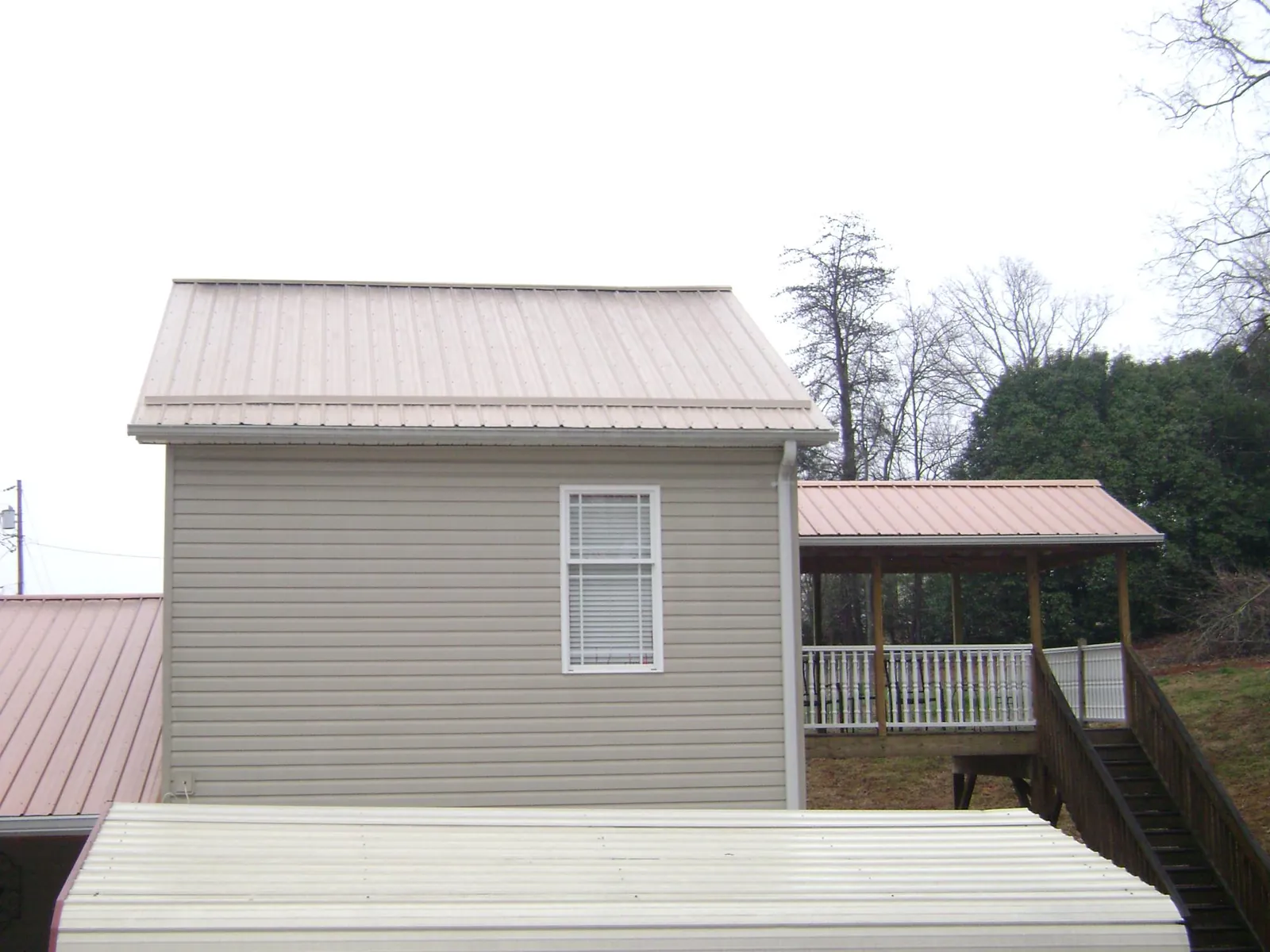Tan metal roofs on a two story addition and attached porch, from a Roof Replacement job in Lakemore